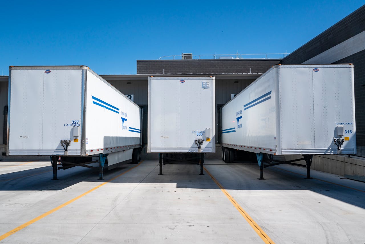 who-we-are Three white cargo trailers parked at an industrial shipping dock under clear blue skies.