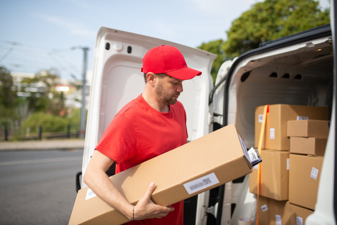 services-01 Courier in red uniform unloading packages from a delivery van on a sunny day.